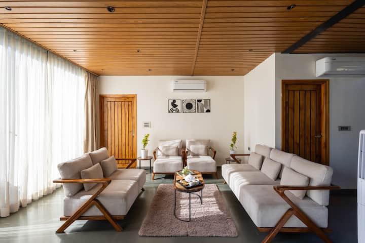 Отпуснете се в нашата осветена от слънцето всекидневна с елегантен дървен таван и модерни места за сядане. Прозрачните пердета от пода до тавана и минималистичният декор създават светло и просторно пространство, идеално за събирания със семейството и приятелите