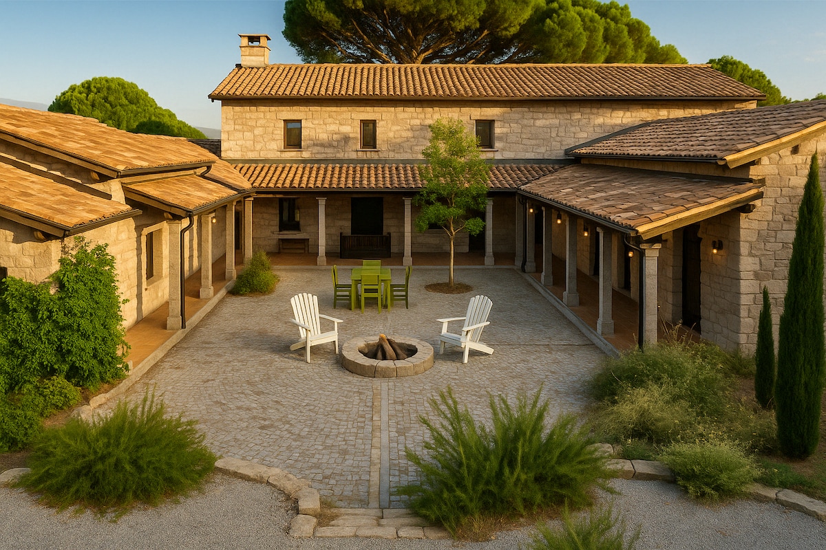 The exterior of a Mediterranean-style home is presented, featuring rugged stone walls and a terracotta roof. A central courtyard with a firepit and seating area is surrounded by well-maintained landscaping. White adirondack chairs complement green tables beneath shady trees.