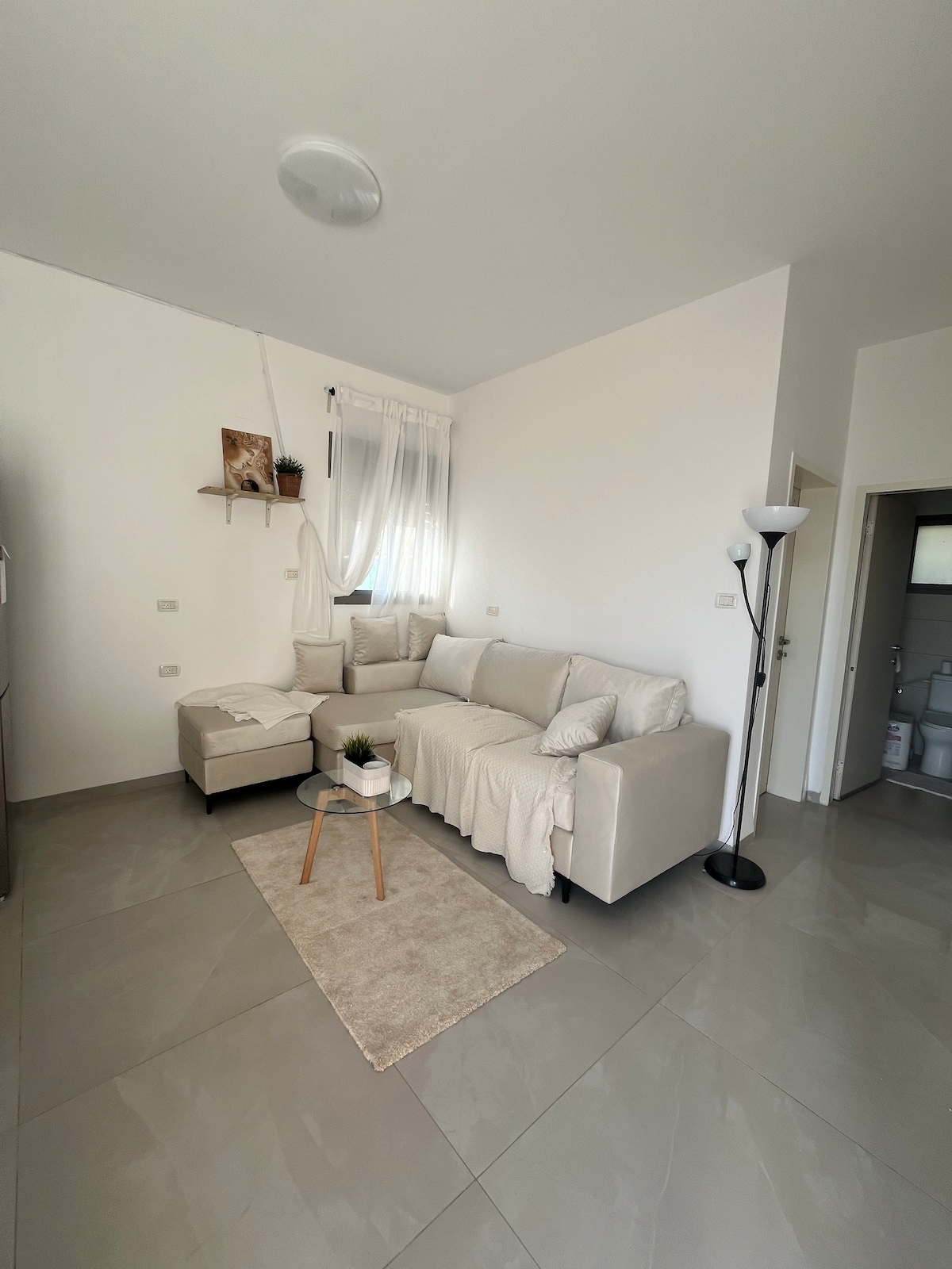 La sala de estar incluye un sofá, una pequeña mesa de vidrio, una alfombra, una manta y cortinas opacas.