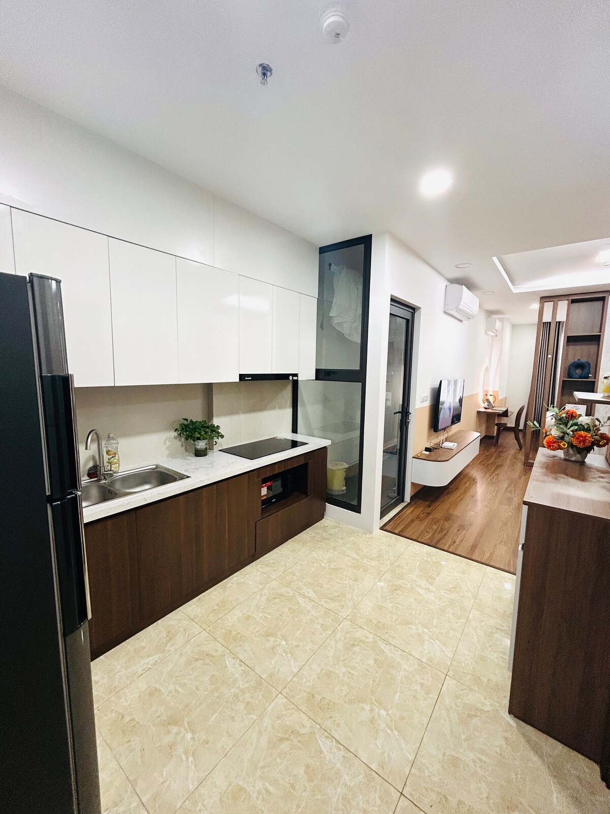 The kitchen features a modern design with light and dark cabinetry, including a sleek refrigerator, a sink, and ample countertop space. The open layout allows for easy access to the adjacent living area, allowing for seamless interaction between spaces.