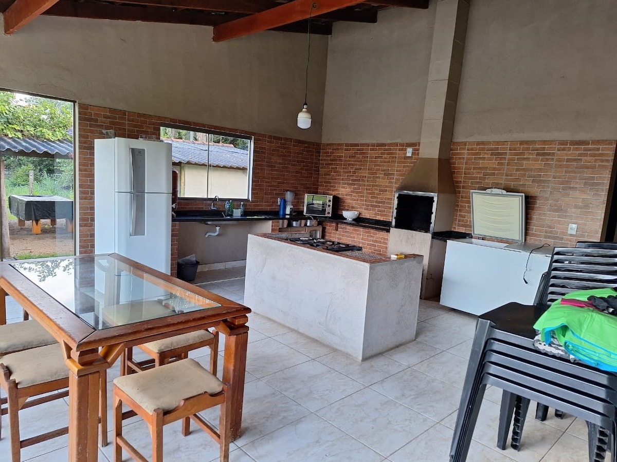 A spacious kitchen area features a central island with a stovetop and ample counter space. A large window allows natural light to flood the room, highlighting the modern appliances, including a refrigerator. A wooden dining table with seating for four complements the space.