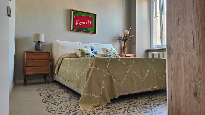 Spálňa s manželskou posteľou pozostávajúca z manželskej postele, 4-dverovej skrine, zrkadla, lampy, nástenného svietidla a dvoch nočných stolíkov. 