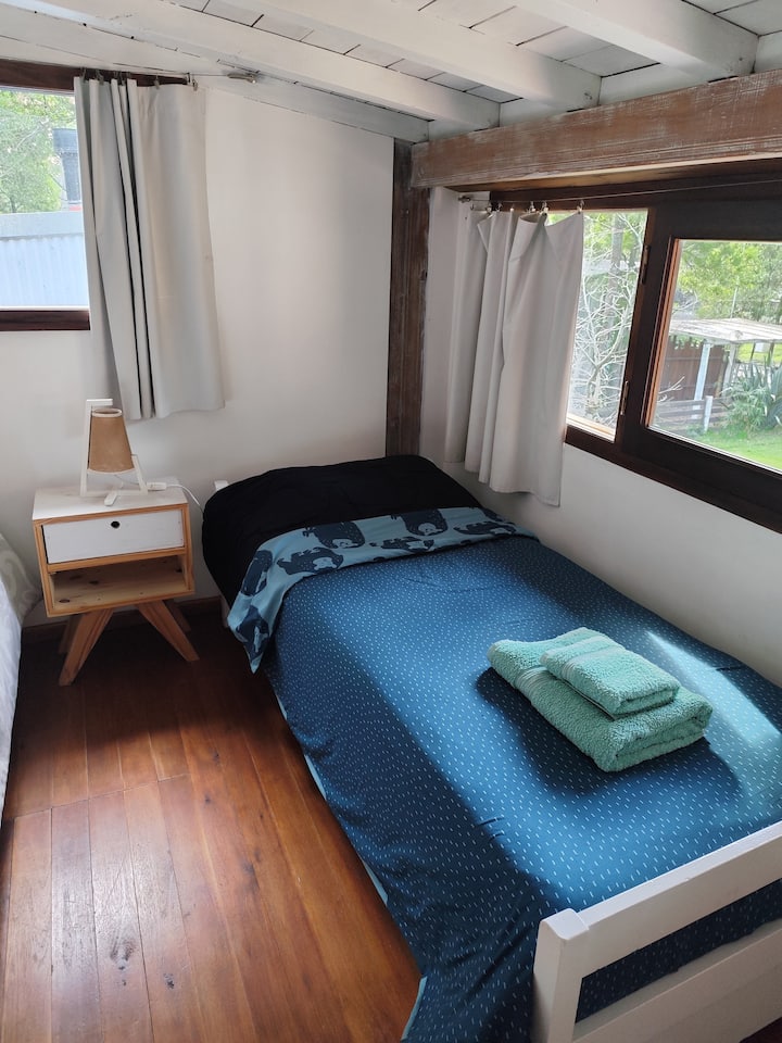 Ოთახი ორი ერთადგილიანი საწოლით და ორადგილიანი საწოლით, ხის იატაკითა და ჭერით, ძალიან ნათელი, უშუქო ფარდებით.