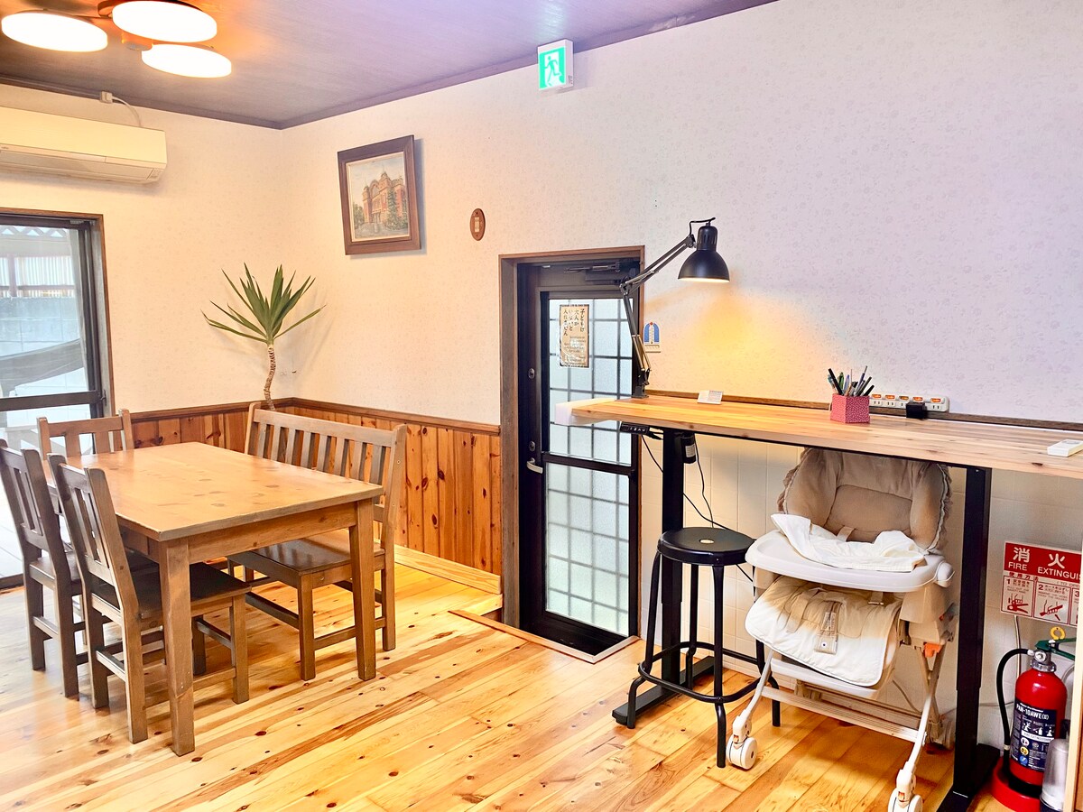 A dining area is featured with a wooden table surrounded by matching chairs. A high chair is positioned near the table, and a bar height table is nearby with a lamp providing light. Natural wood accents enhance the warm atmosphere of the space.