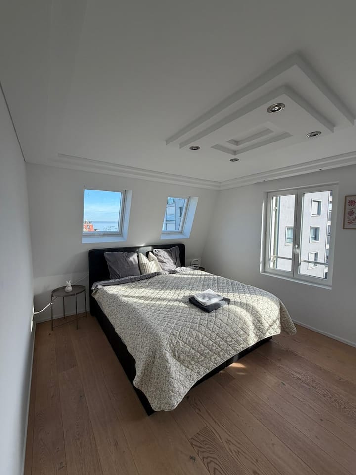 غرفة نوم مشرقة وحديثة بسيطة مع سرير كبير 180 × 200 سم، والكثير من ضوء النهار من خلال ثلاث نوافذ كبيرة ومفروشات واضحة وهادئة.