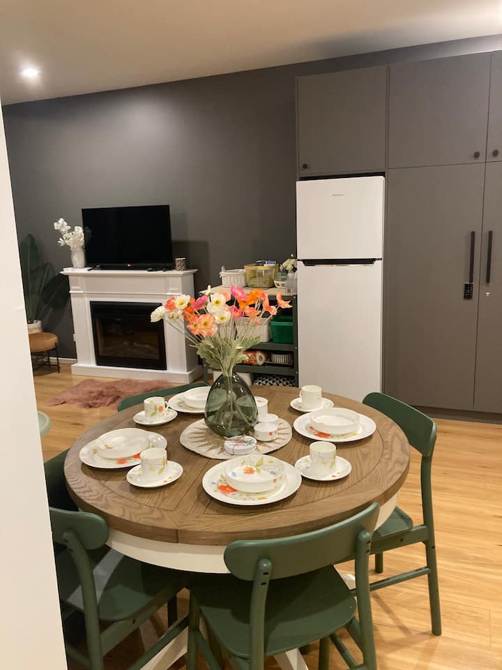 Mesa de comedor con 5 sillas, todos los platos y tazas, etc. 
Una silla plegable más está al lado del pequeño banco de la isla junto a la nevera.