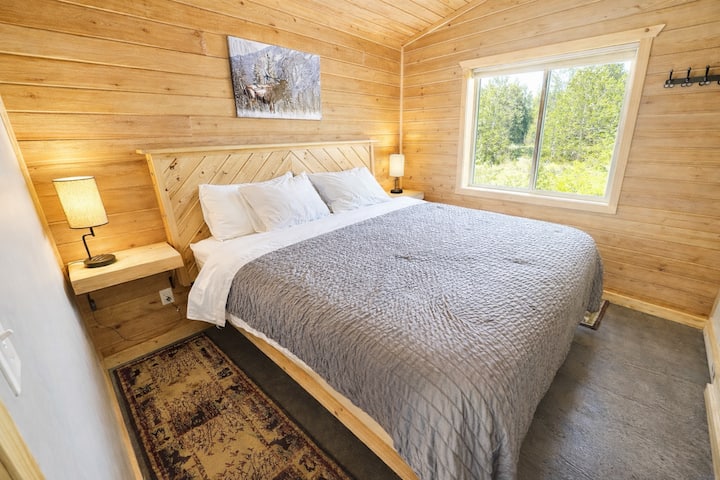Chambre confortable de style cabine avec lit king size, tables de chevet avec lampes et murs en bois naturel.