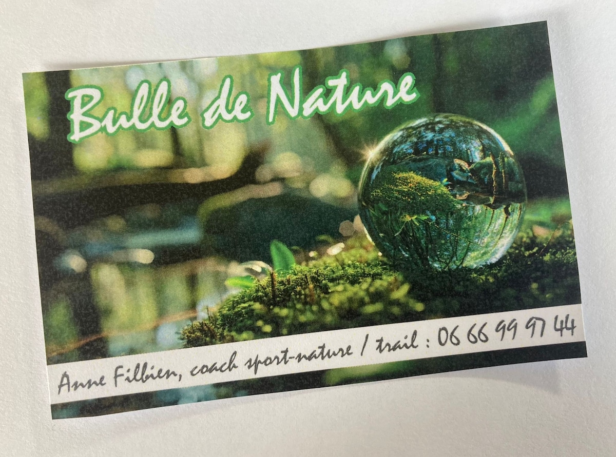 A business card is displayed, featuring a close-up image of a crystal orb resting on a moss-covered surface. The orb reflects the surrounding greenery, creating a peaceful natural atmosphere. The text includes the name 'Bulle de Nature' and contact information for nature coaching services.