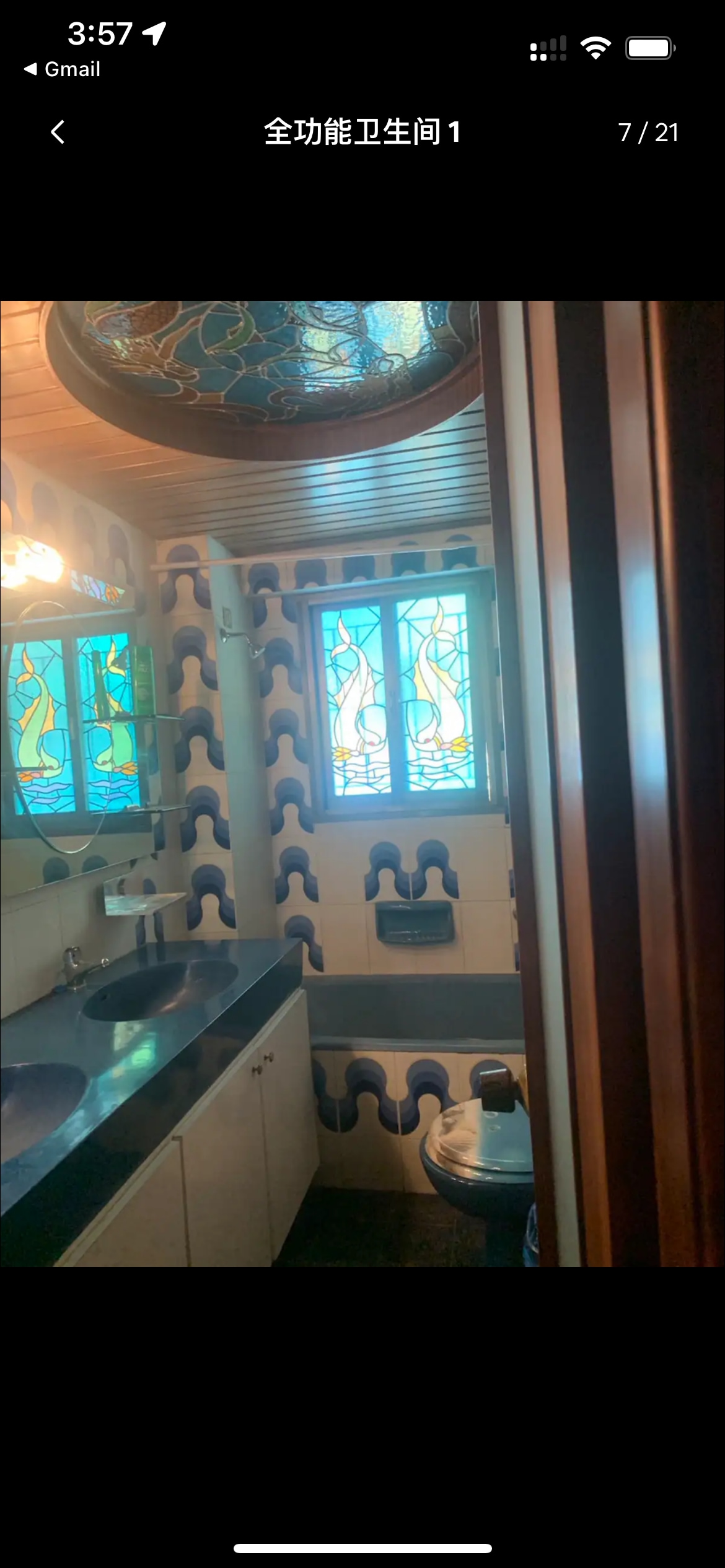A brightly decorated bathroom features intricate stained glass windows that allow natural light to filter in. A modern sink and dark countertop provide functional elegance, while patterned ceramic tiles add texture to the walls. A view of the toilet and bathtub is also visible.