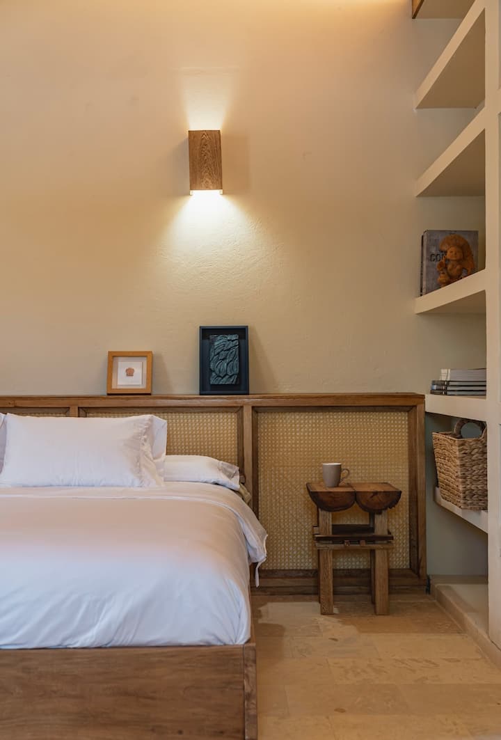 Habitación rústica de estilo caribeño con detalles naturales, muebles de madera y tonos cálidos. Incluye una cama tamaño king y cuatro camas individuales, perfectas para familias o grupos que buscan comodidad y tranquilidad en un ambiente tropical acogedor.