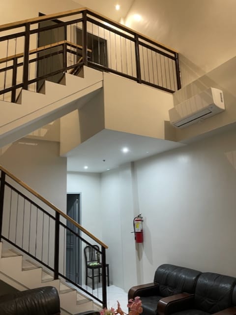A modern staircase leads to an upper level, showcasing a clean design. Bright lighting enhances the open space, while a comfortable seating area with a dark leather couch is positioned on one side. An air conditioning unit is mounted above, ensuring a comfortable climate.