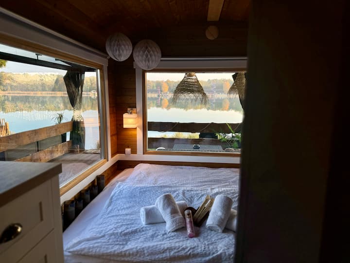 En el dormitorio puedes acurrucarte en una cama de 1,60 x 2,00 m. Las dos grandes ventanas panorámicas te dan las mejores vistas del lago. También encontrarás suficiente espacio para tus pertenencias aquí en una cómoda y un sistema de armario abierto.