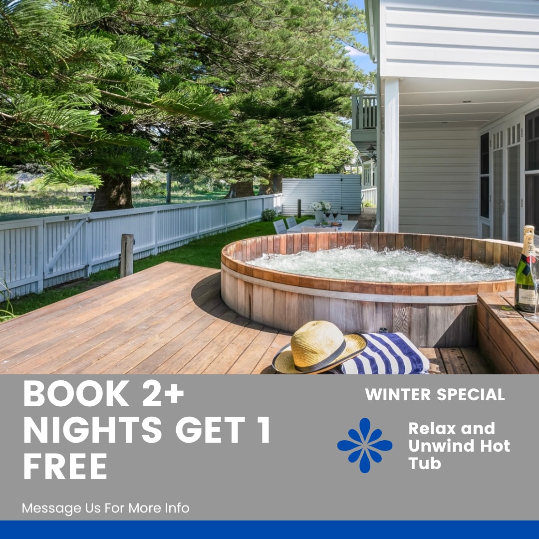 A wooden hot tub is positioned outdoors on a deck surrounded by greenery and fencing. It features bubbling water, inviting guests to relax. A sun hat rests nearby, suggesting a tranquil atmosphere. The property offers a peaceful outdoor setting for unwinding.