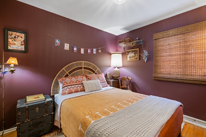 Orient Express–inspired bedroom, featuring a plush queen bed, rattan headboard, and rich plum tones for a luxurious, old-world feel.