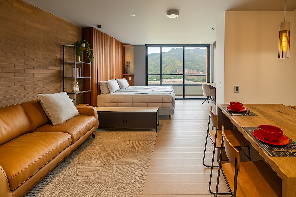 A spacious loft area features a large king bed with crisp linens, an inviting leather sofa, and a stylish dining table set for four. Floor-to-ceiling windows offer views of the surrounding hills, while soft lighting enhances the modern interior design.