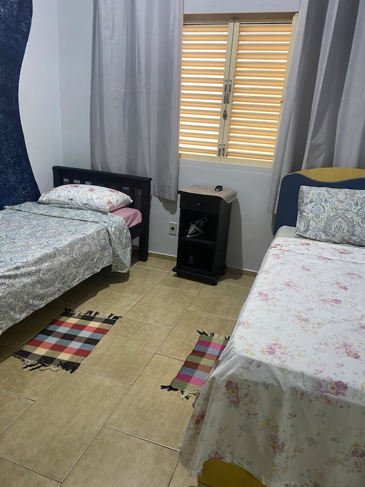 غرفة نوم بسريرين مفردين وطاولة للكي وخزانة ملابس وملابس ولحاف وبطانية ومناشف