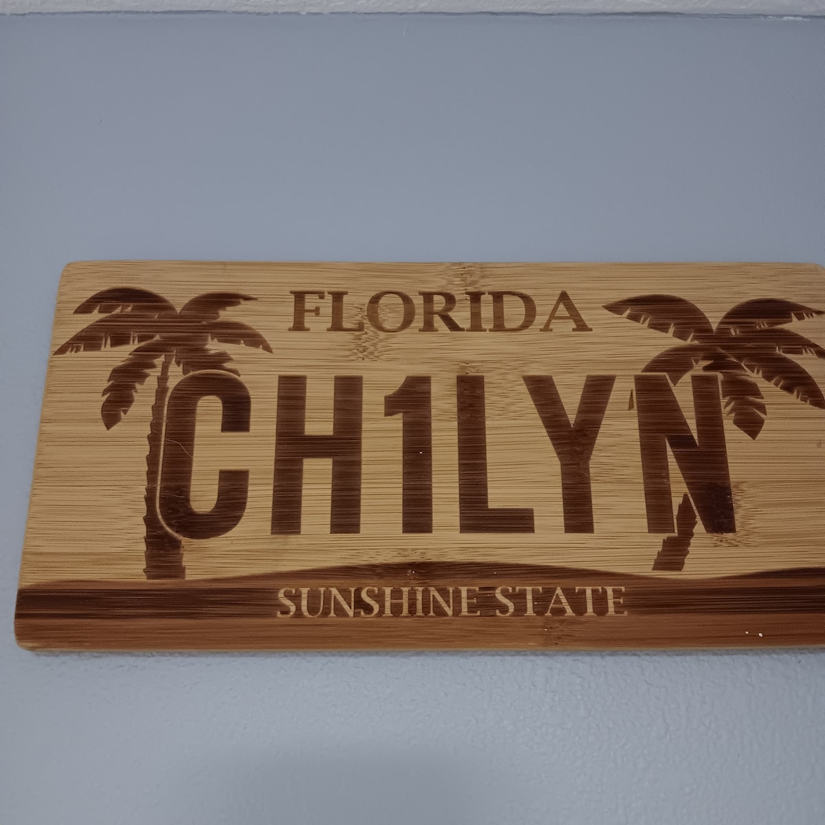 A decorative wooden sign is displayed on the wall, featuring the words 'Florida CH1LYN' and 'SUNSHINE STATE.' Palm tree silhouettes are engraved on either side, creating a distinct and welcoming element that reflects the local culture.