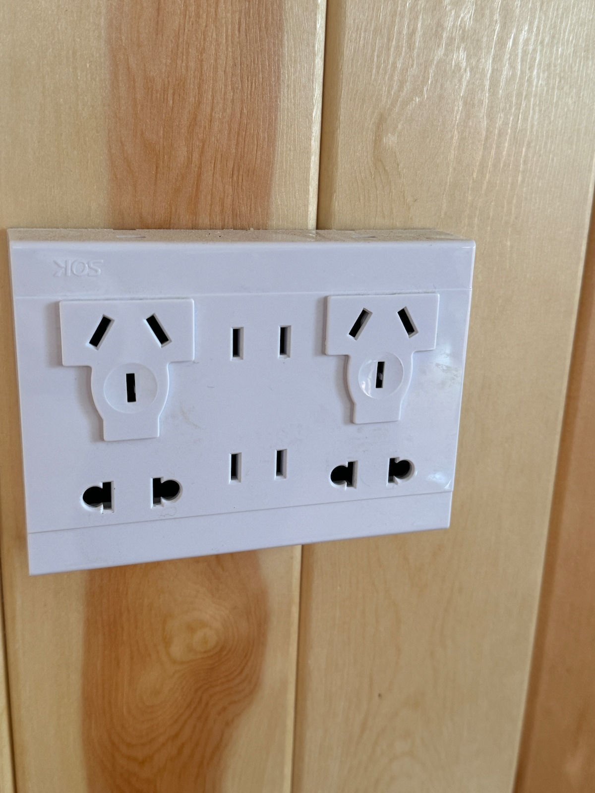 A clean, modern electrical outlet is mounted on a light wooden panel. The design features multiple sockets, accommodating different plug types for convenience.