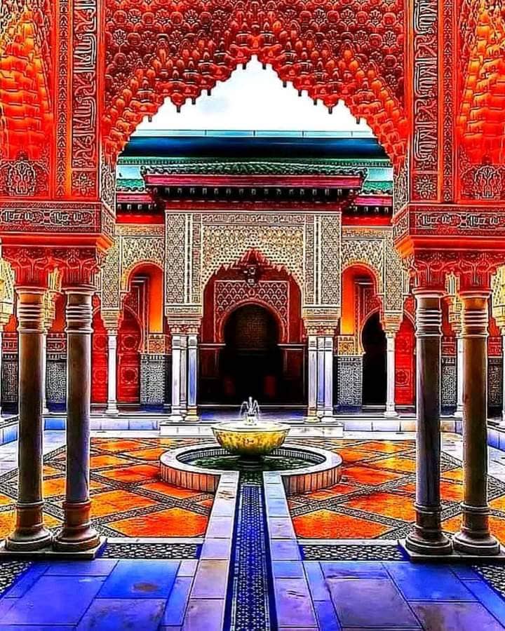 An intricately designed courtyard features vibrant tiled patterns and detailed archways, with columns supporting the ornate ceiling. A central fountain, surrounded by colorful tiles, adds a calming focal point to the serene outdoor space.