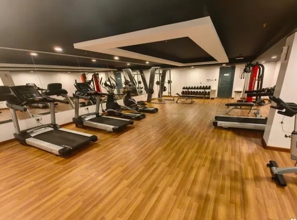 A well-equipped gym is presented, featuring several treadmills and weight machines. Mirrors line one wall, enhancing the sense of space. The wooden flooring contributes to a warm atmosphere, and various weight lifting equipment is organized neatly, ready for use.