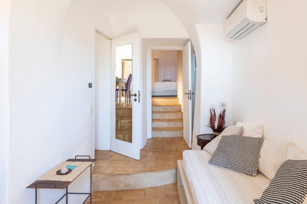 Sala de estar con sofá cama individual, TV, aire acondicionado y entrada independiente que conduce a un área de relajación a la sombra.