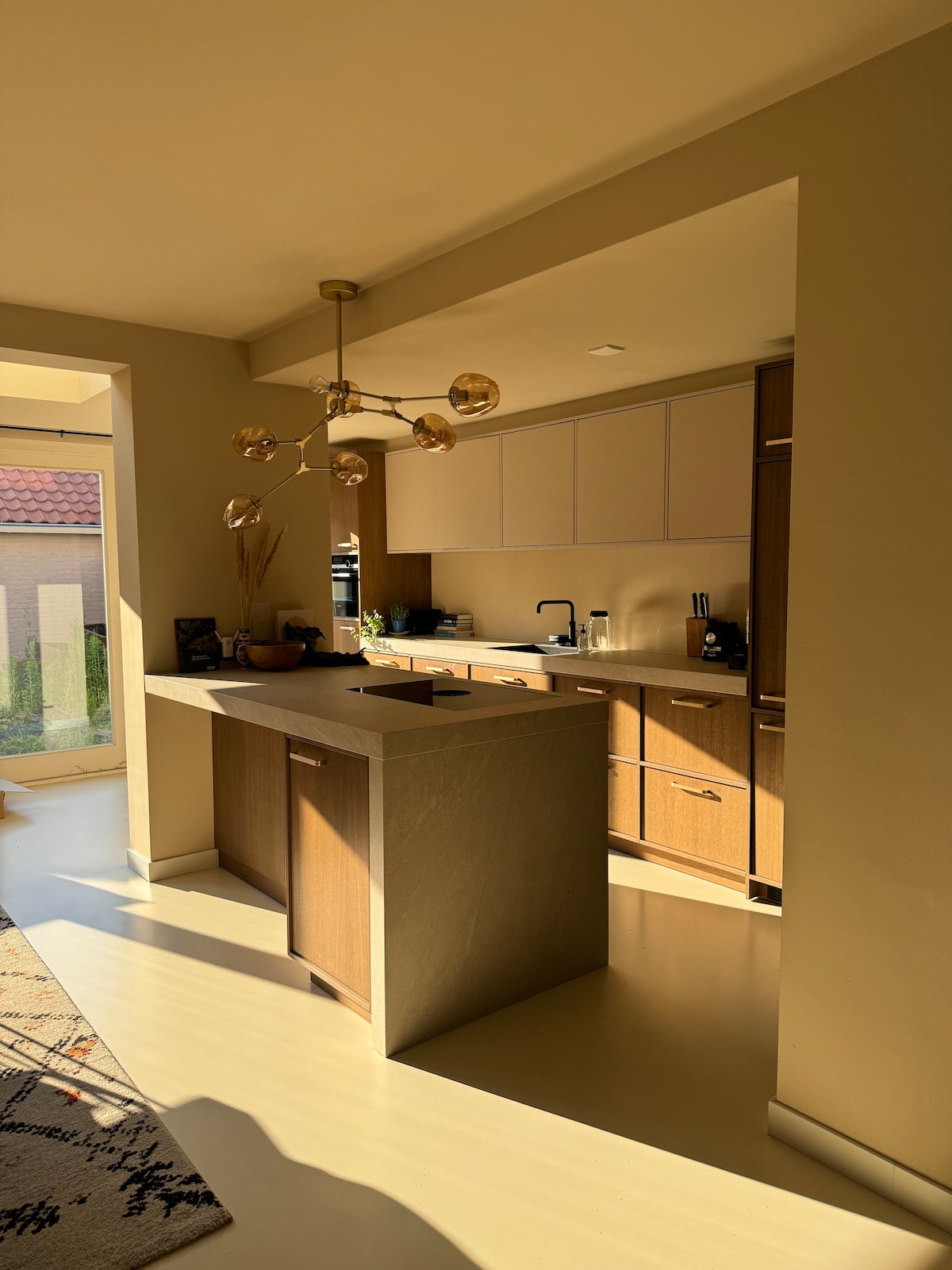 A well-equipped kitchen is displayed, featuring modern cabinetry and a central island. Natural light illuminates the space, highlighting the minimalist design. Countertop appliances and utensils are arranged neatly, creating an organized and inviting cooking area.
