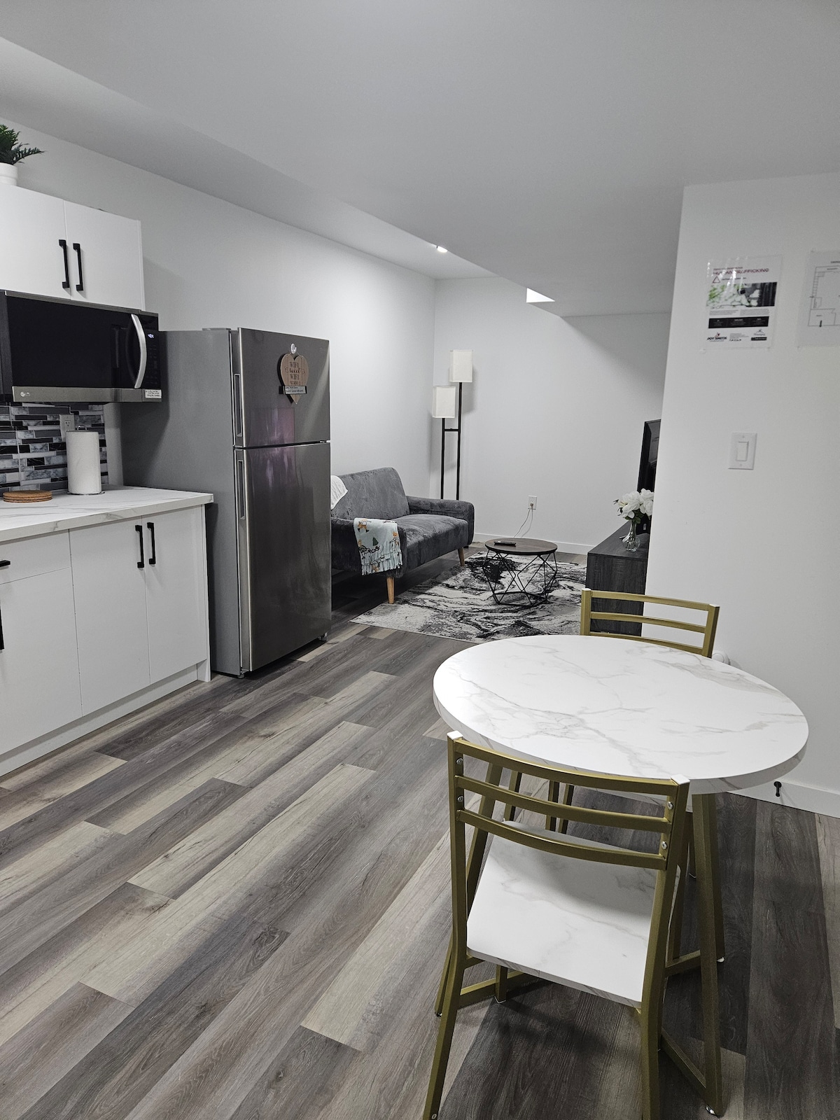 A modern kitchen area features sleek cabinetry and stainless steel appliances. A small dining table with two chairs is positioned nearby, providing a cozy space for meals. A comfortable sofa is visible in the background, complemented by soft lighting and a simple area rug.