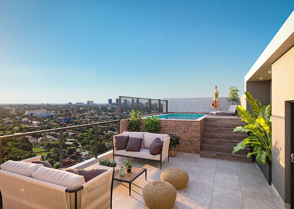 An outdoor terrace is featured with modern lounge seating and two round poufs. A swimming pool is visible, surrounded by a glass railing. Green foliage adds a touch of nature. The city skyline is seen in the background against a clear sky.