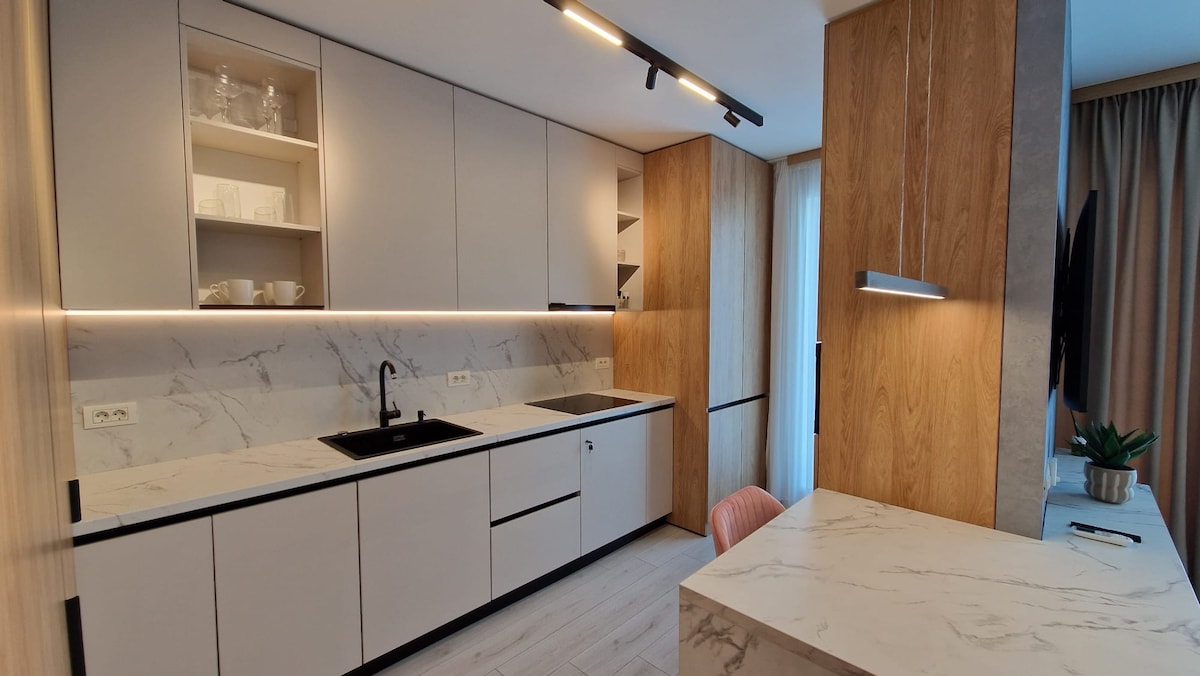 A modern kitchen is presented with sleek cabinetry, featuring a combination of light and dark finishes. A marble countertop complements the minimalist design, with essential appliances visible. Soft lighting highlights the space, enhancing the functional layout suitable for meal preparation and dining.