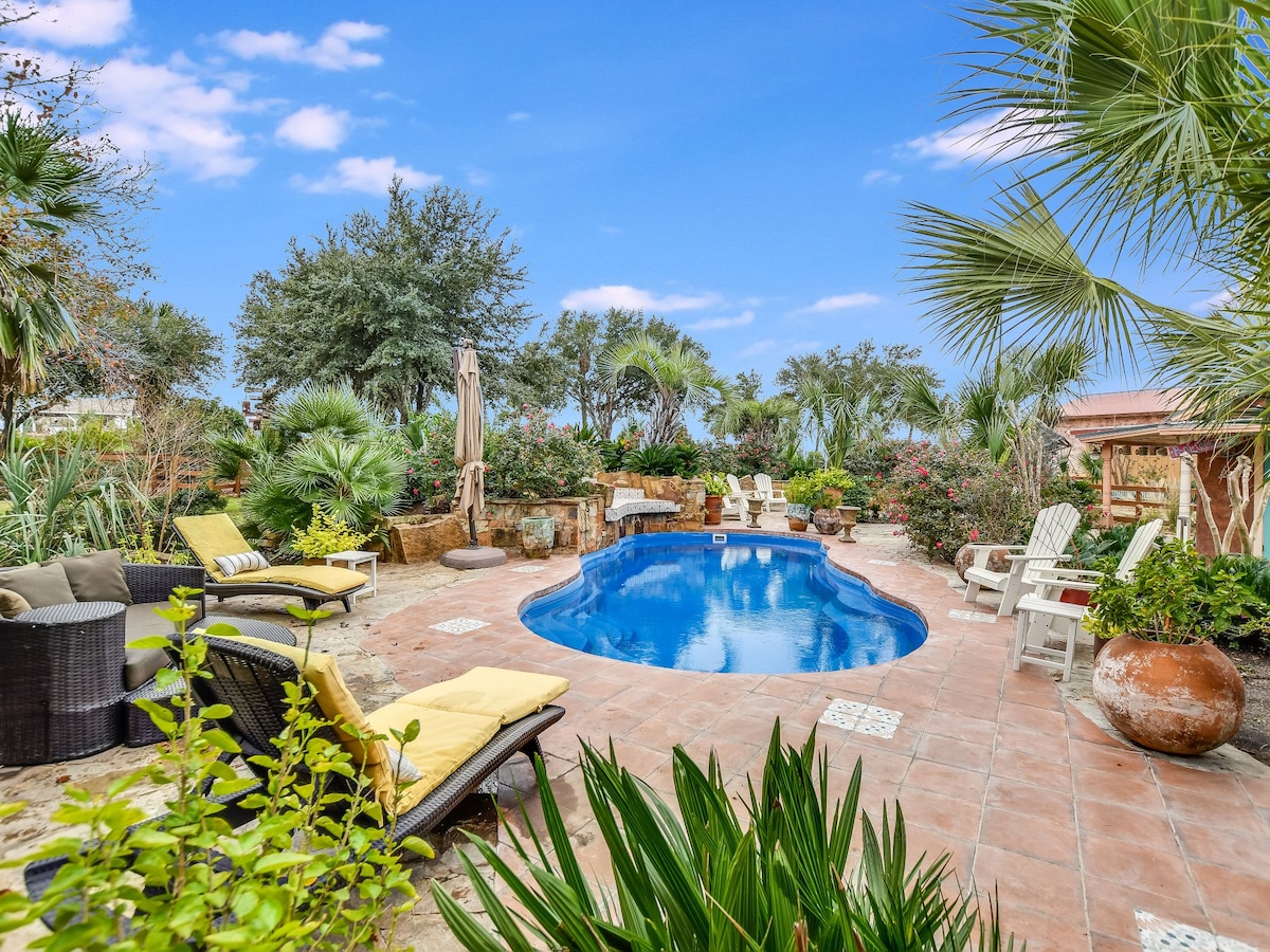 A private outdoor pool is surrounded by lush greenery, featuring lounge chairs and small tables for relaxation. The area is complemented by various plants, creating a tranquil oasis. Sun loungers are positioned strategically around the pool for comfort and leisure.