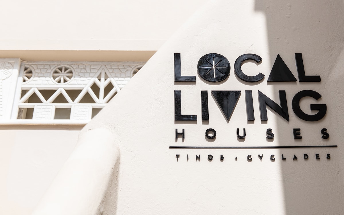 The exterior signage of Local Living Houses is prominently displayed, featuring a modern design. The sign is black against a light wall, situated above an elegantly crafted architectural detail that includes circular shapes and a geometric pattern. Soft, natural light highlights the elements.