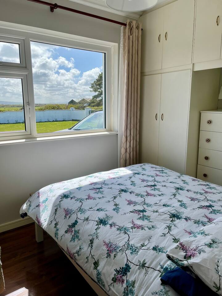 这张双人床可俯瞰前面的草坪和远处的山脉。 房间里有一个衣橱、一张边桌和一面手拿镜子。 