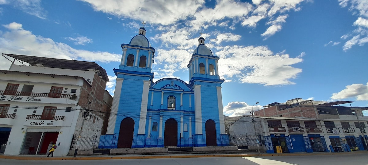A historic blue church is prominent against a clear sky, featuring twin domed towers and an arched entrance. Nearby buildings with colonial architecture are visible, framed by the expansive open square and scattered clouds above, adding to the charm of the location.