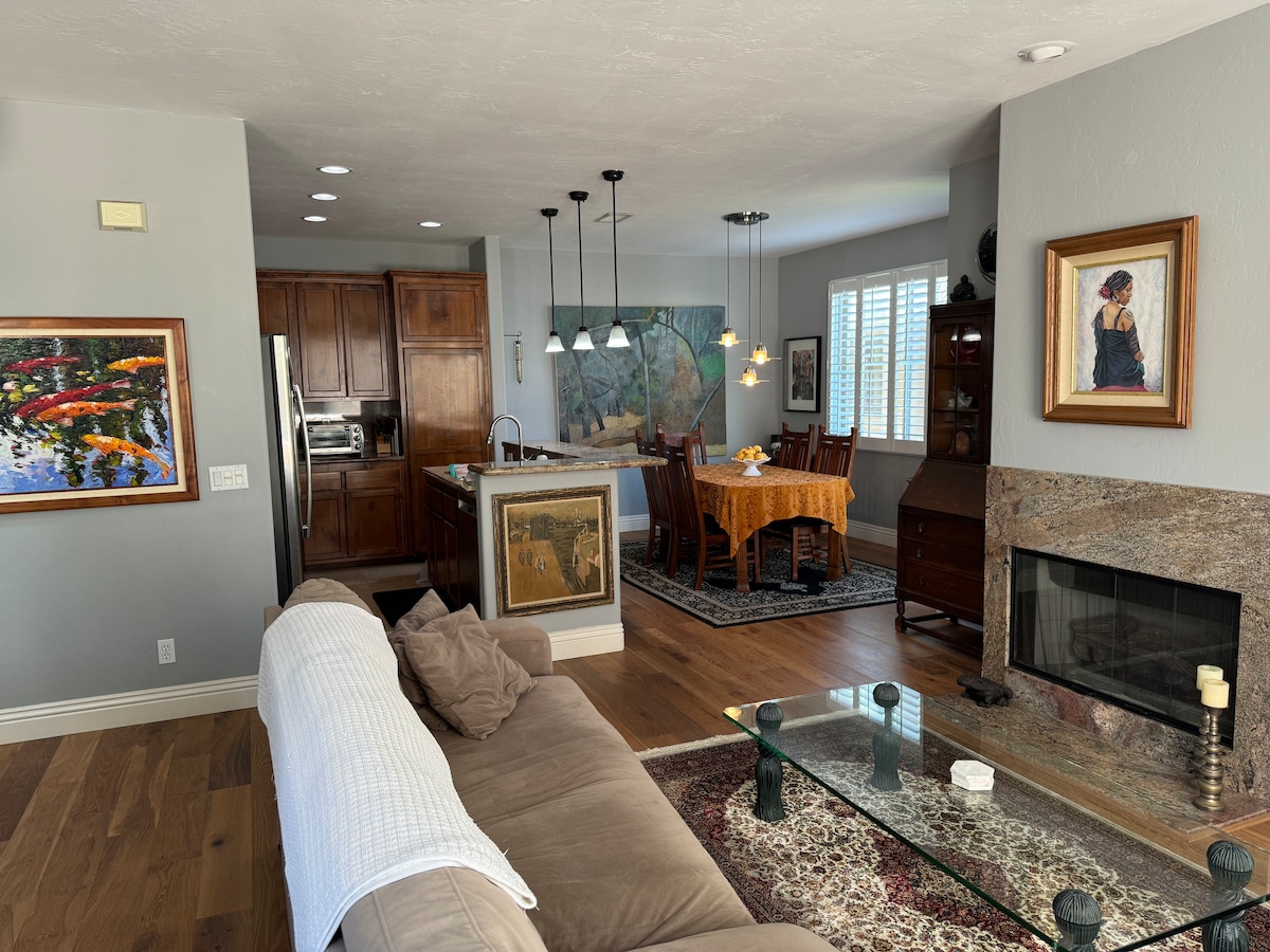 The open living space features a comfortable sofa and a coffee table positioned in front of a fireplace. A dining area with a table is illuminated by pendant lights, and artwork adorns the walls, adding a touch of creativity to the environment.