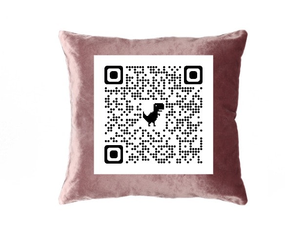 A soft, pink velvet pillow is displayed prominently, featuring a contrasty black and white QR code centered on its surface. The smooth texture of the pillow complements the starkness of the code, providing an inviting touch to the space.