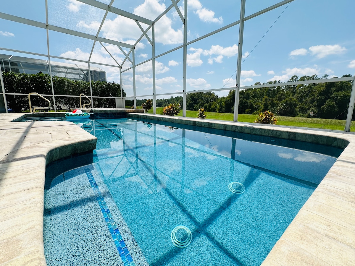A private pool is showcased, surrounded by a screened enclosure. The clear water reflects sunlight, and the shallow entry steps provide accessibility. Lush greenery is visible beyond the pool area, enhancing the serene ambiance of the outdoor space.