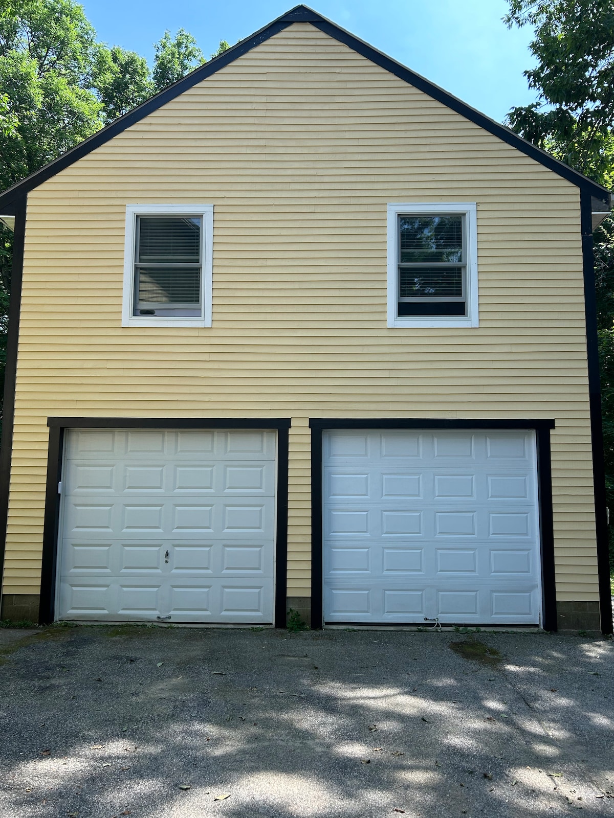 A two-story structure is presented, featuring a light yellow exterior with white trim. Two garage doors are located on the ground level, each exhibiting a simple design. Above, a pair of windows allow natural light into the upper level.