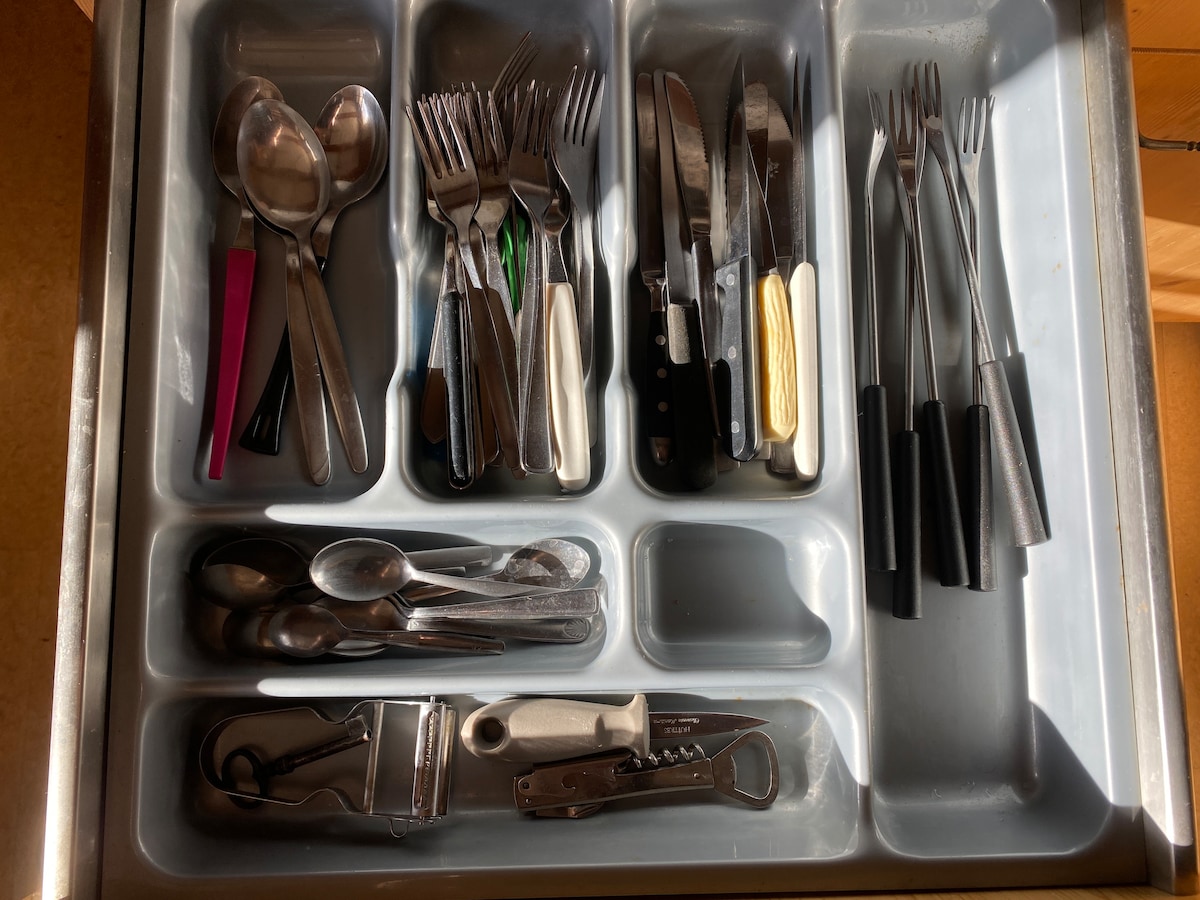 A silverware drawer is neatly organized, featuring various utensils including spoons, forks, knives, and additional tools. The items are displayed in separate compartments, with a few uniquely colored utensils adding subtle contrast to the metallic tones.