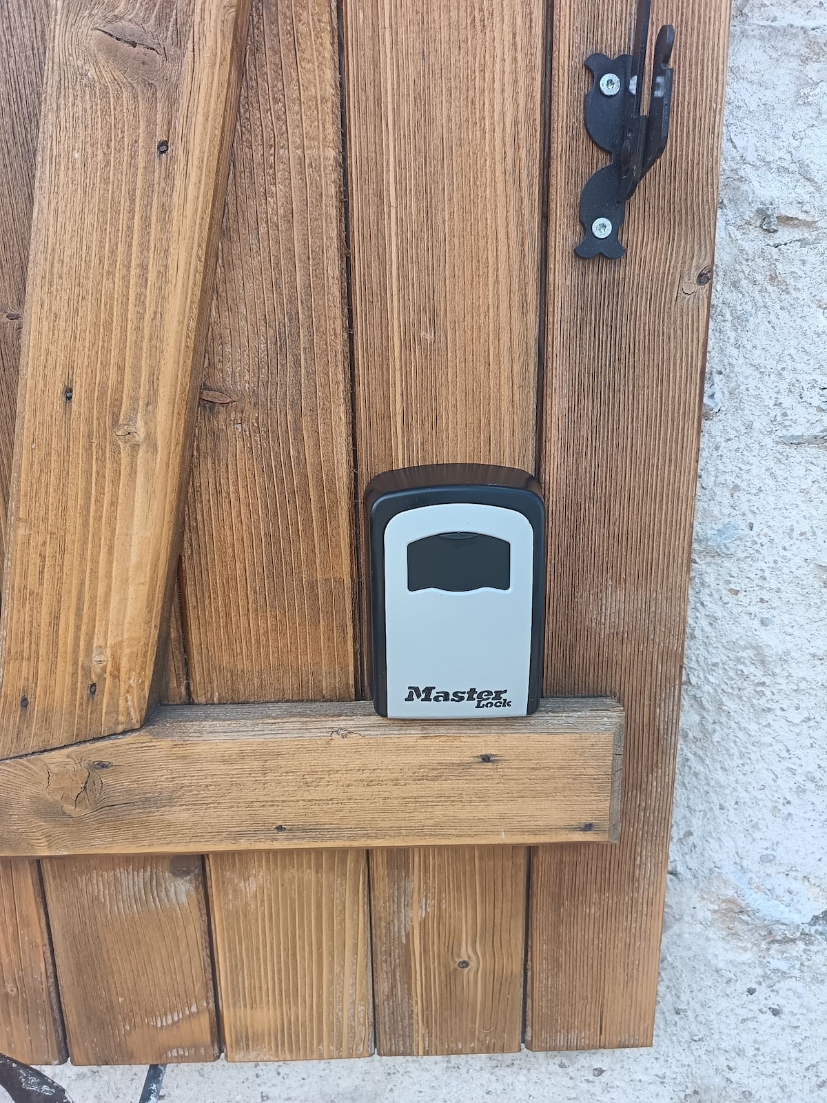 A secure key storage box is mounted on a wooden door, offering a practical solution for access. The wooden door features a rustic design with natural grain visible, complemented by a metal latch beside the box.