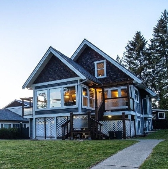 A two-story house with a distinct architectural style features large windows that allow natural light to fill the interior. The exterior showcases a combination of dark siding and light detailing, with a welcoming entrance consisting of a staircase leading to a private patio area.