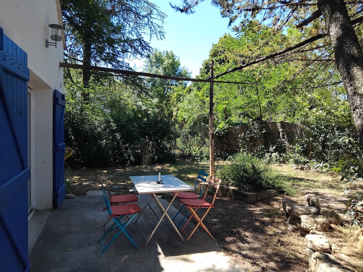 An outdoor dining area is featured with a spacious table surrounded by colored chairs. Lush greenery and trees provide a natural setting, while a clear blue sky is visible overhead. The area offers a serene environment for meals or relaxation.