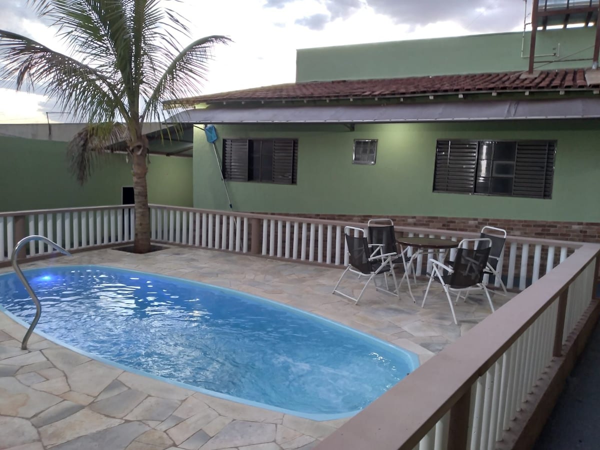 A private pool is surrounded by natural stone flooring and a wooden fence. Two lounge chairs are positioned near the pool, accompanied by a small table. A palm tree stands to one side, adding a touch of greenery to the outdoor space.