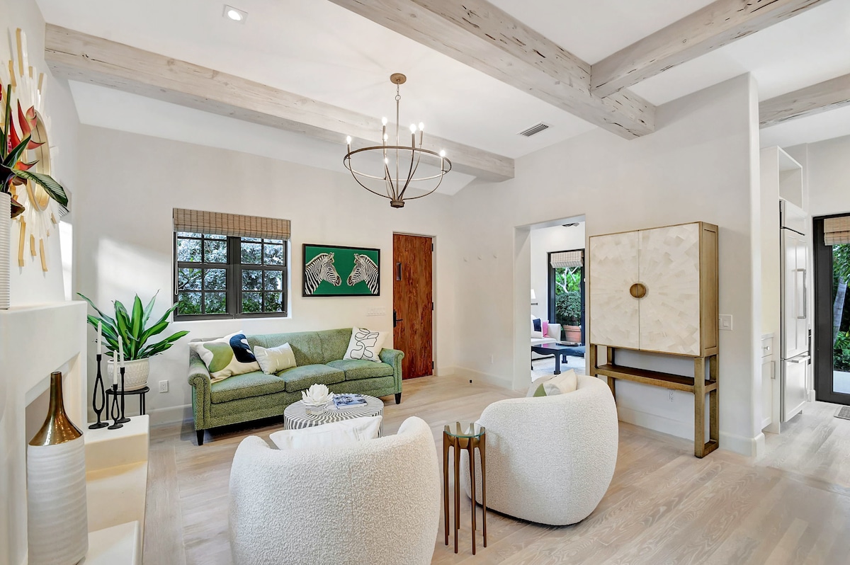 Living room with arched entry to the den, pecky cypress entry door, and decorative cabinet — light-filled and open to the outdoors.
