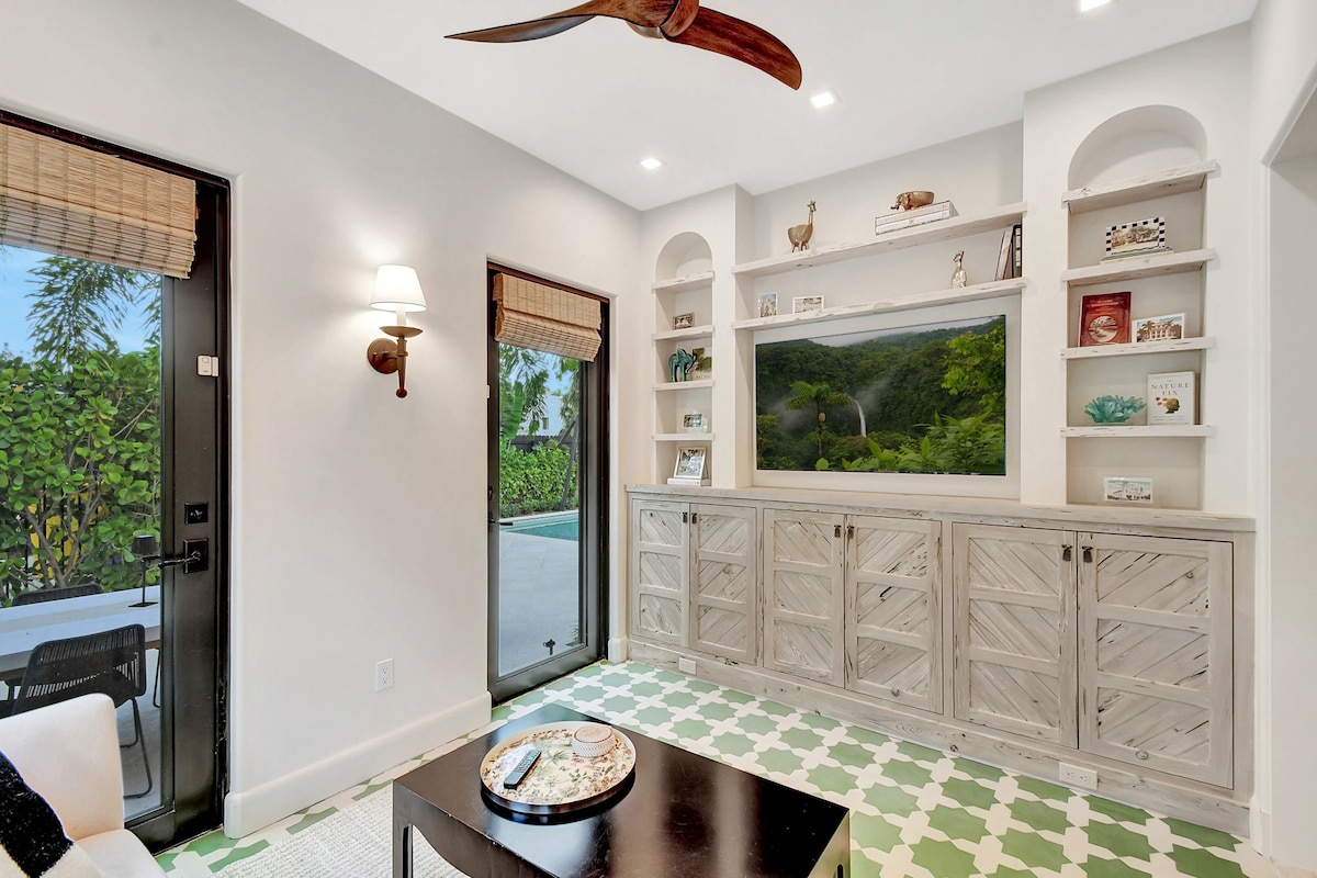 Den's built-in pecky cypress cabinetry and shelving frame the smart TV, with glass doors bringing in natural light and glimpses of the patio and pool.