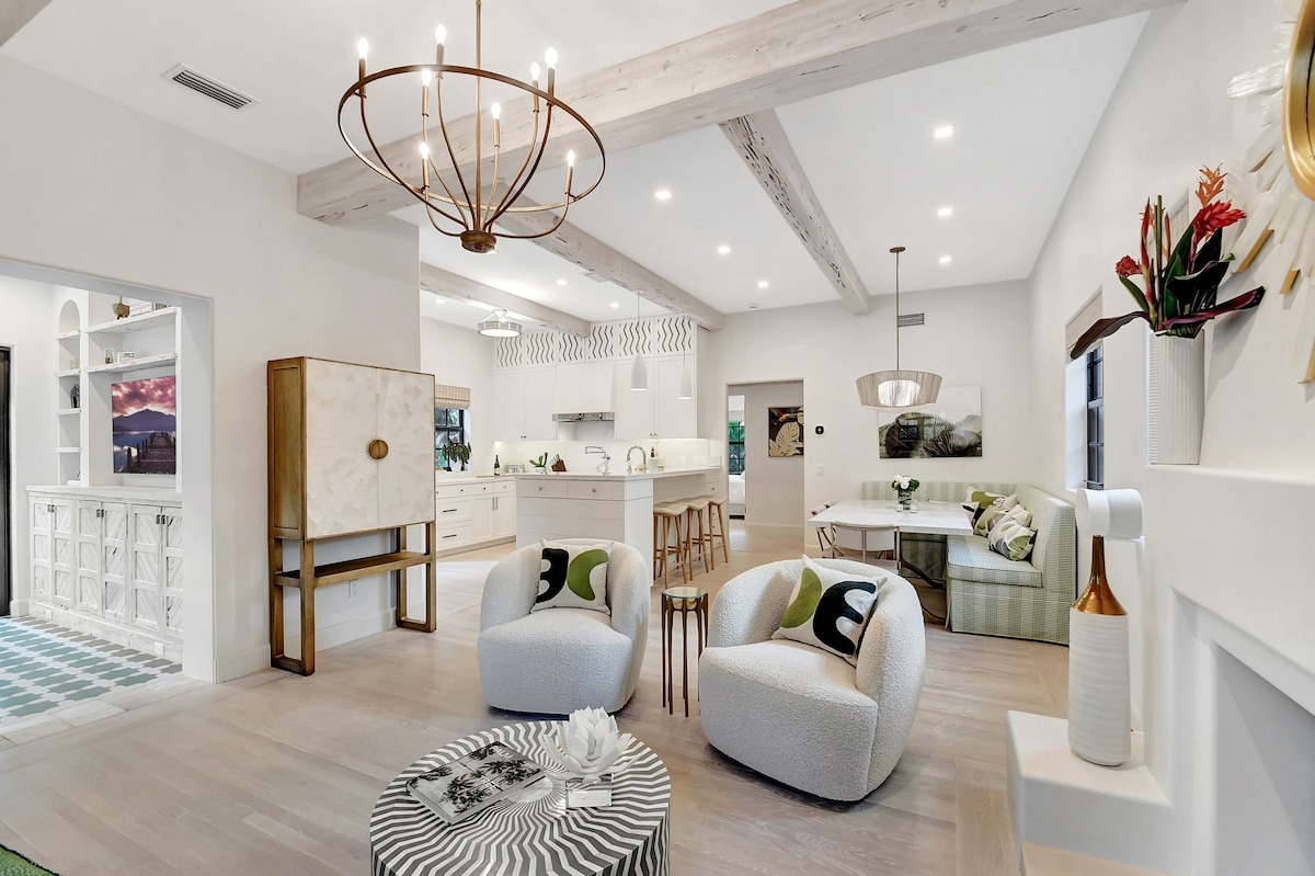 The open floor plan from living room through dining banquette to kitchen — exposed beams and consistent light hardwood flooring connecting every space.