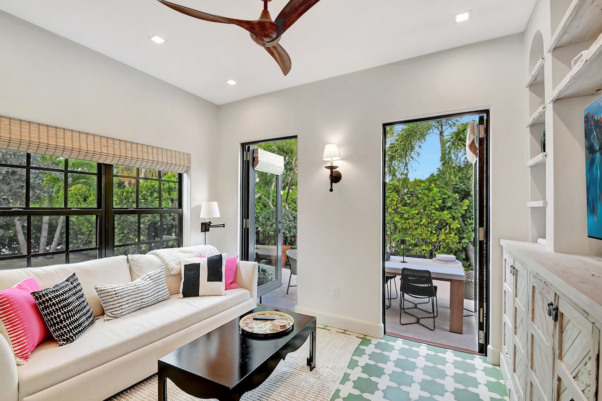 Bright, sunny den with smart TV, built-in shelving, and double doors opening directly to the outdoor dining patio — ideal for morning coffee or an evening drink.