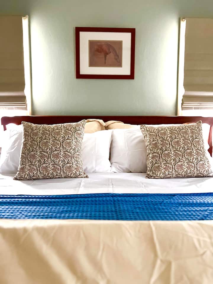 Una acogedora cama tamaño king con una antigua mecedora de madera hace de este dormitorio de esquina un lugar cómodo para descansar y relajarse.  Armario de almacenamiento para ropa y equipaje. 