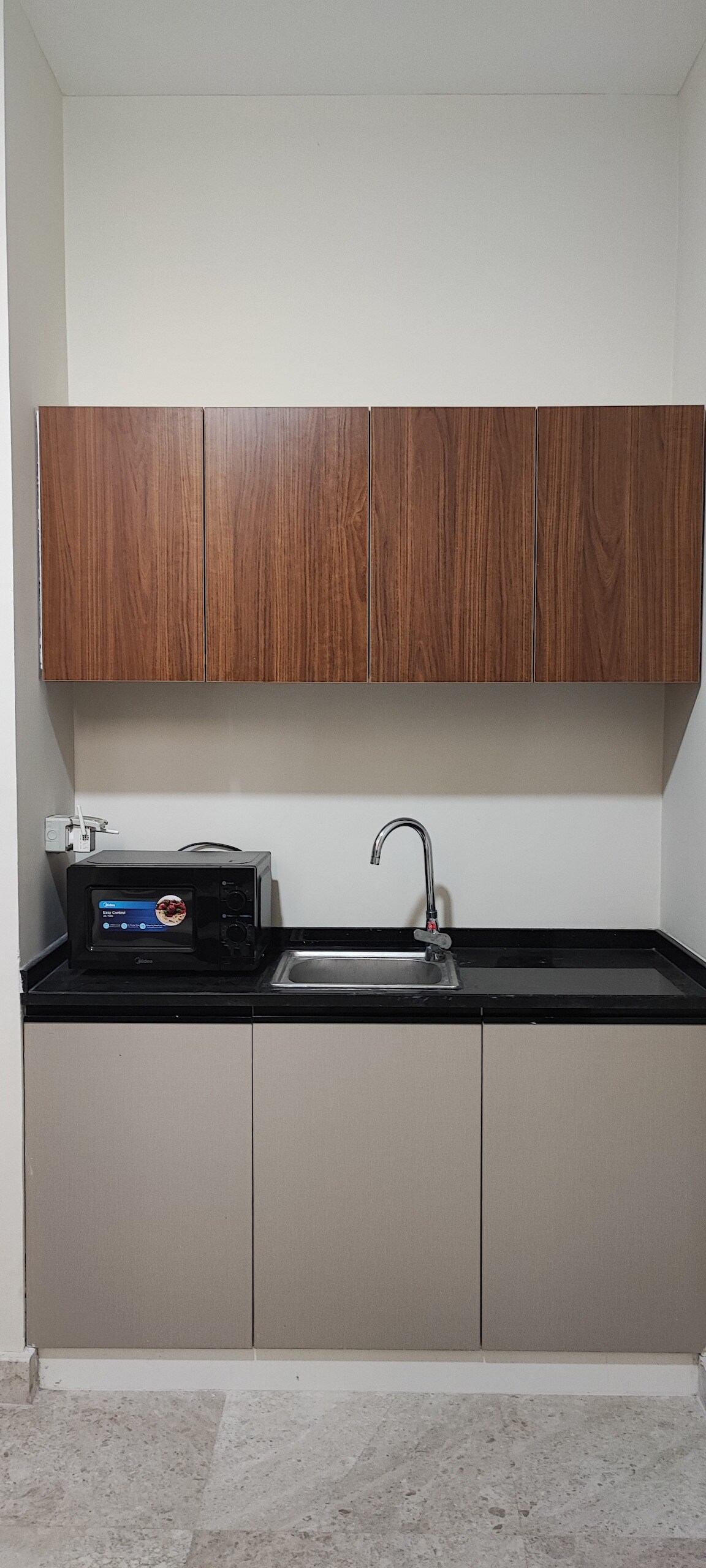 The kitchen area features sleek cabinetry with a wood finish above a modern countertop. A sink is positioned under a wall-mounted cabinet, with a microwave and a small appliance visible on the countertop, providing essential amenities for cooking and dining.