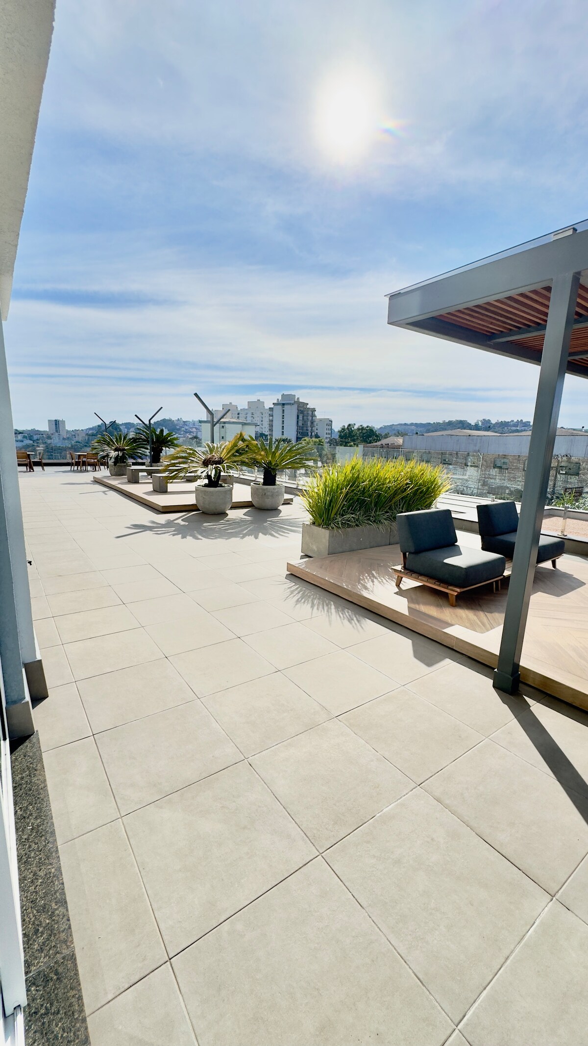 An expansive terrace features sleek outdoor furniture and potted greenery, providing a relaxed setting. The view showcases cityscape elements, with sunlight casting a warm glow across the tiled surface. This open area allows for a variety of outdoor activities.
