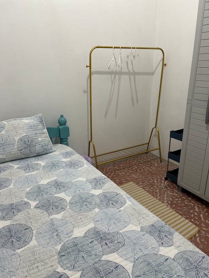 Habitación #3 cuenta con cama de 1 plaza, abanico de pared, área para colgar ropa, ventanas con tela metálica y cortinas. 